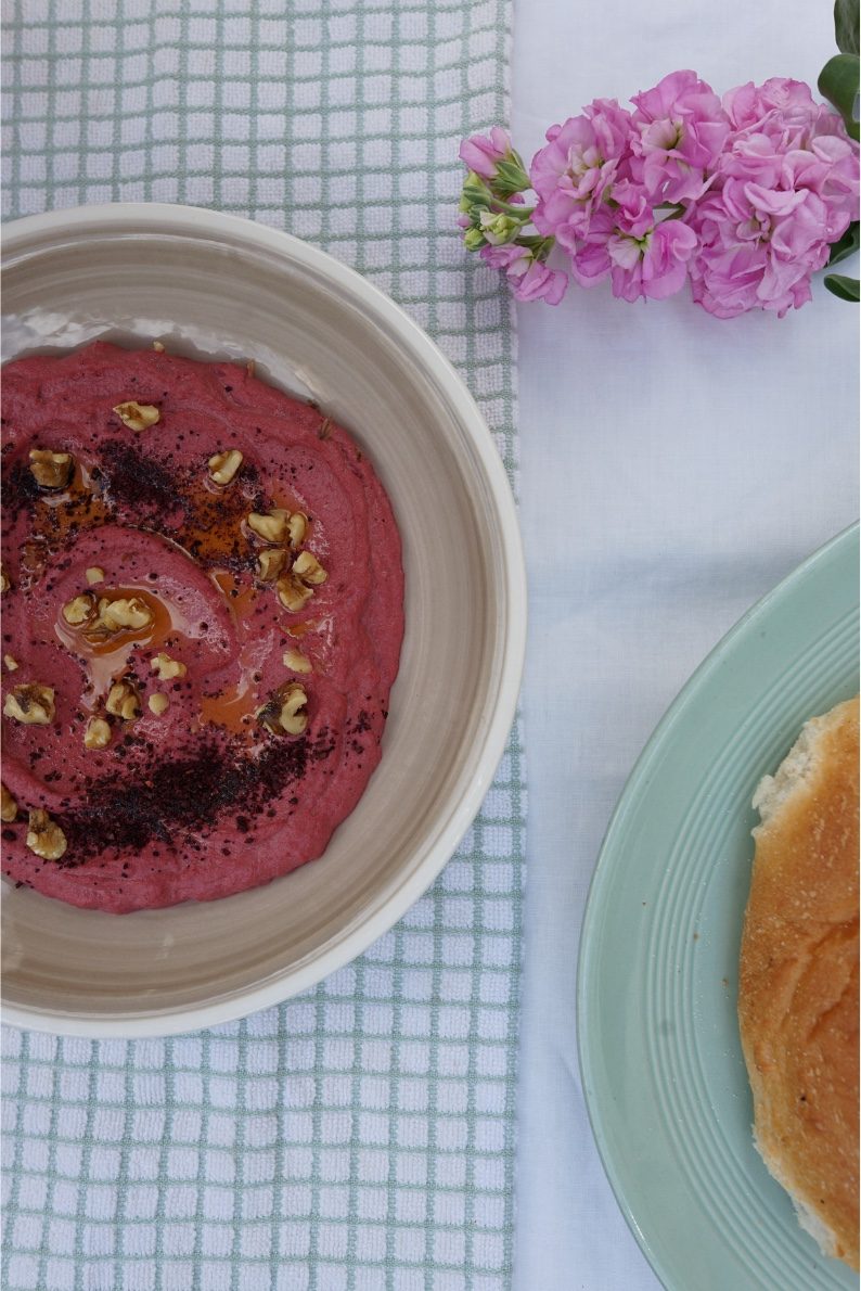 Beetroot and walnut dip with sumac beside pink stock flowers and a round of bread