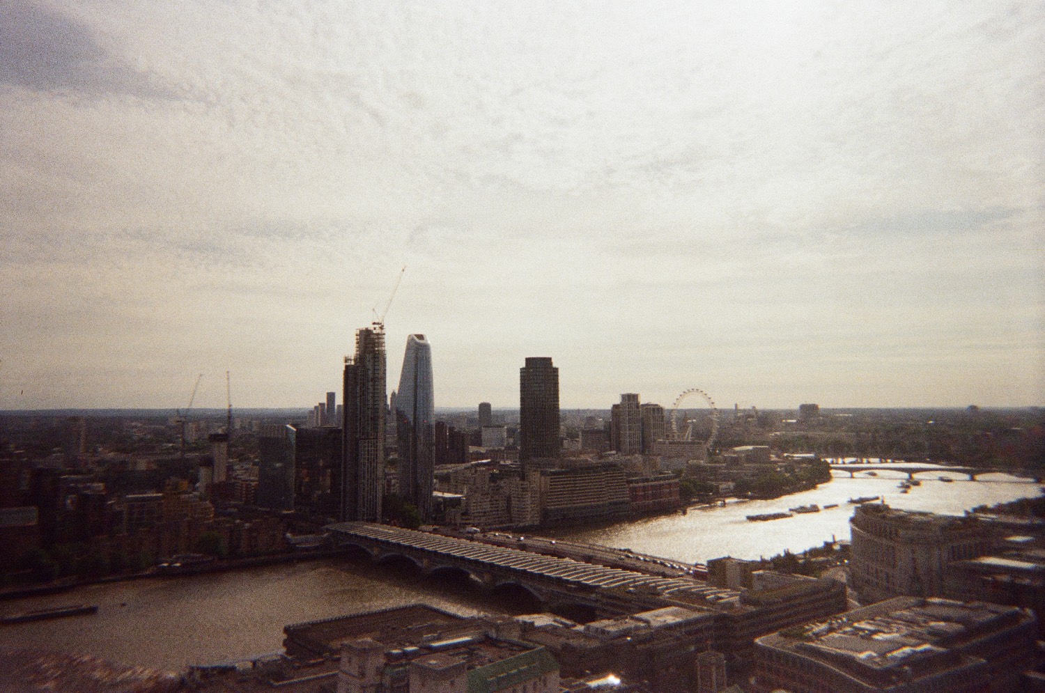 The River Thames and the London skyline seen from high up, with bridges, tower blocks and the London Eye under a hazy sky